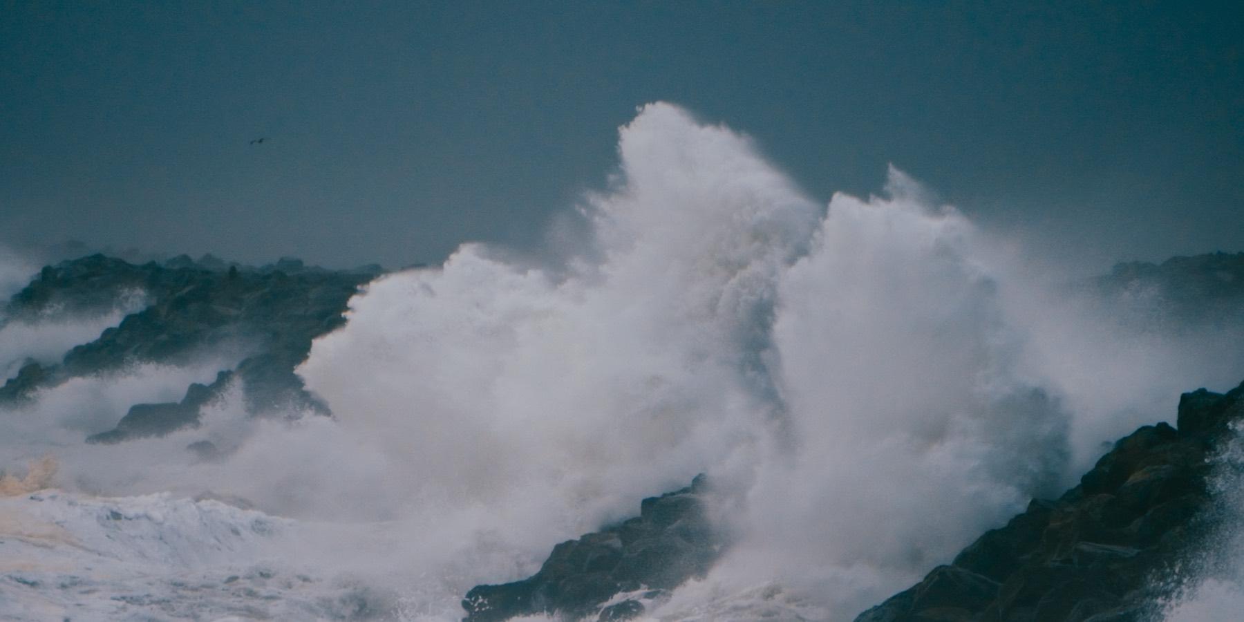 A storm swell breaks white over dark basalt at the mouth of the Columbia River.