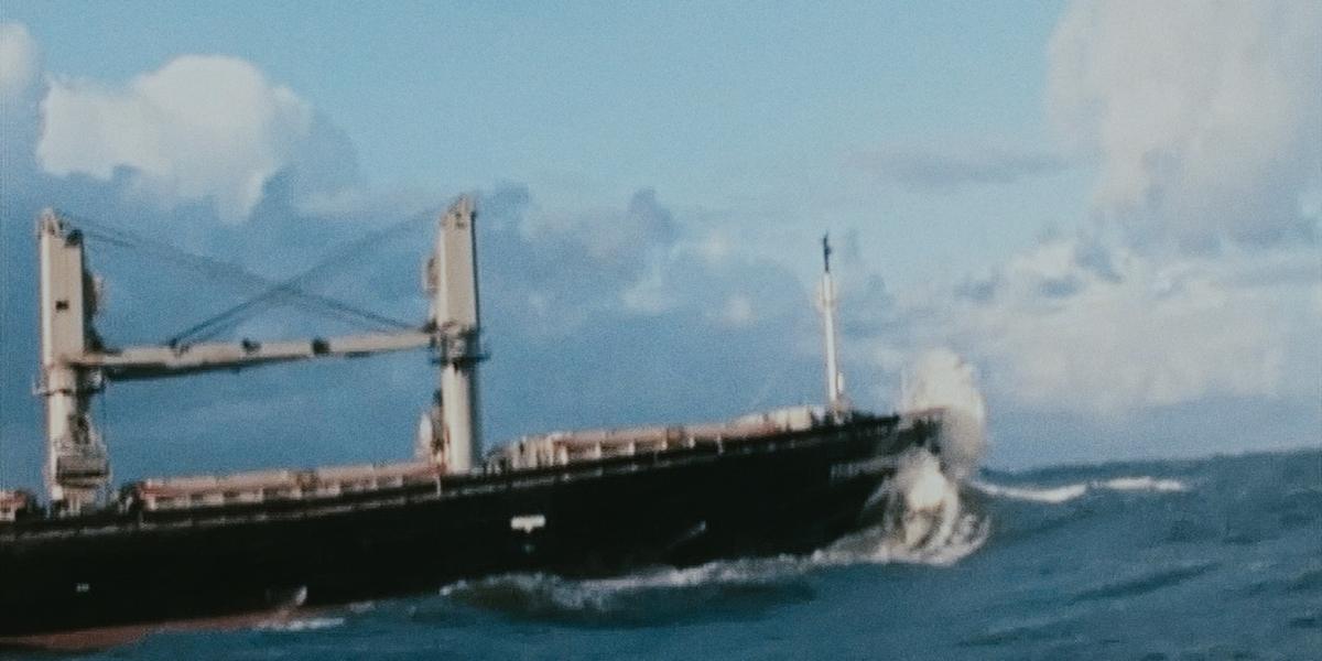 A cargo ship plows through breaking surf on the bar.